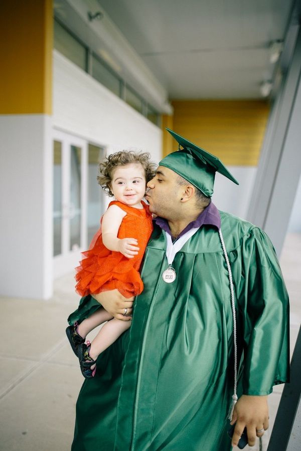 Luis Tolentino in graduation gown, holding a toddler. Credit: Goodwill Excel Center Central And Southern Indiana