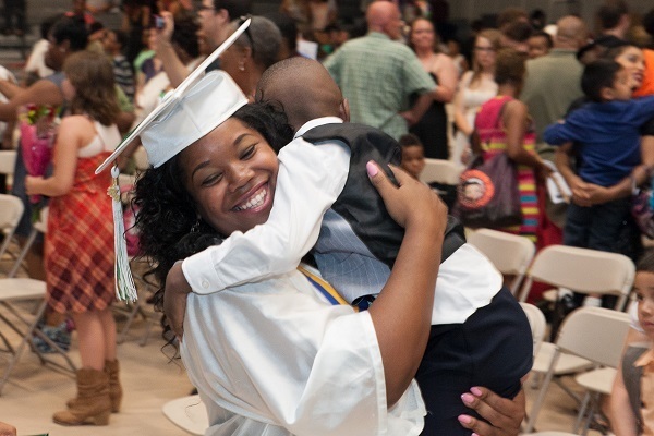 A woman in graduation cap and gown hugging her young son