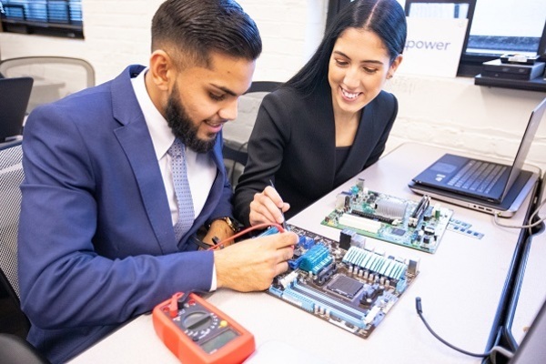 A young man and young woman working on a school technology project at a table