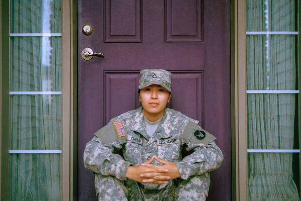 A young female military veteran sitting in front of the front door to her house