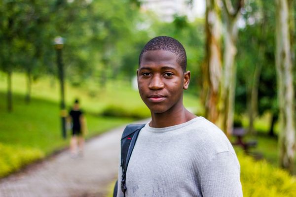 Black male teenager carrying a backpack and standing in a park