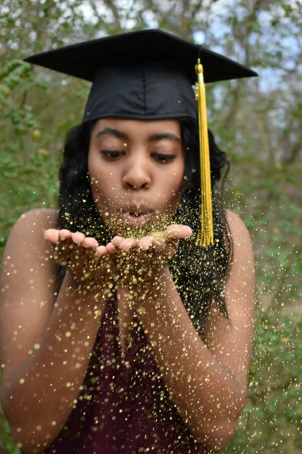 A woman wearing a graduation cap blowing glitter out of her hands