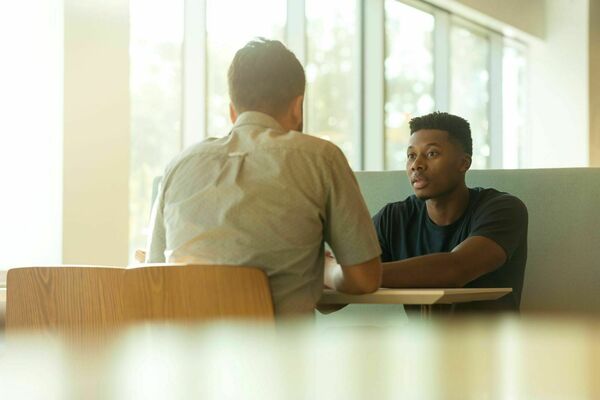 A young man sitting at a table talking to a mentor